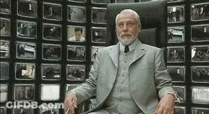 A Man In A Suit Is Sitting In Front Of A Wall Of Televisions . GIF
