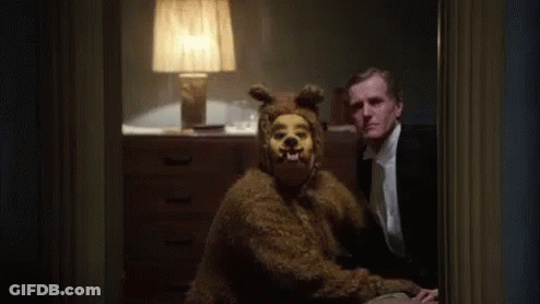 A Man In A Suit Is Sitting Next To A Bear Costume . GIF