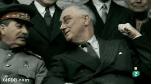 A Man In A Suit Is Sitting Next To A Man In A Hat With The Number 2 On The Bottom Right GIF