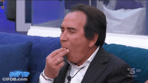 A Man In A Suit Is Sitting On A Blue Couch With #Gfvip Written On The Bottom Of The Screen GIF