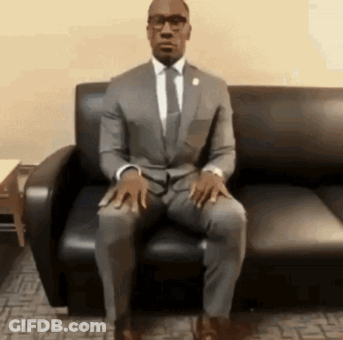 A Man In A Suit Is Sitting On A Couch . GIF