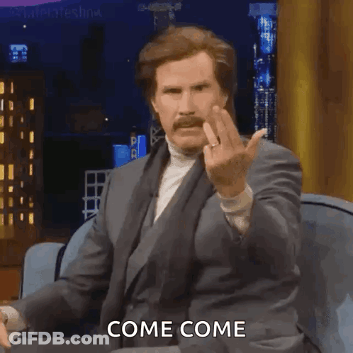 A Man In A Suit Is Sitting On A Couch And Giving The Middle Finger While Saying Come Come GIF