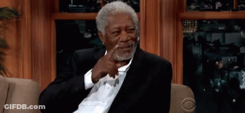 A Man In A Suit Is Sitting On A Couch And Pointing At Himself GIF