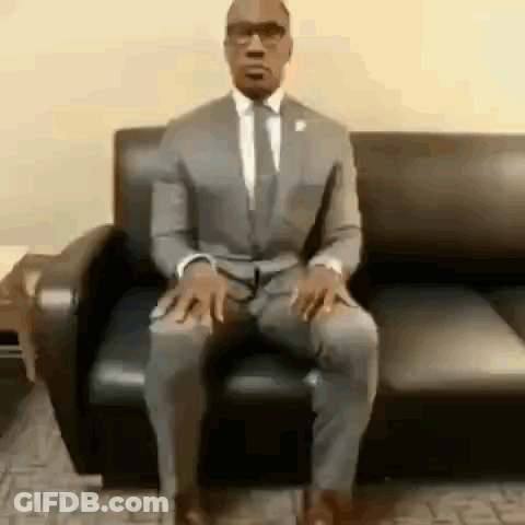 A Man In A Suit Is Sitting On A Couch . GIF