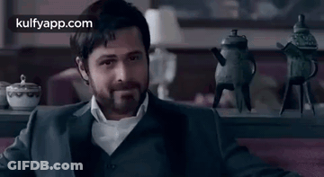 A Man In A Suit Is Sitting On A Couch In Front Of A Table With Teapots On It . GIF