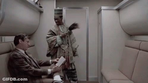 A Man In A Suit Is Sitting On A Couch Next To A Man In A Poncho . GIF
