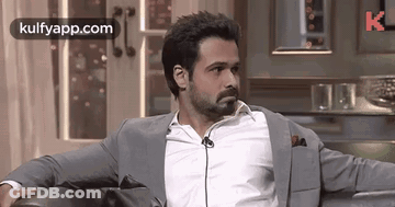 A Man In A Suit Is Sitting On A Couch With His Arms Crossed . GIF