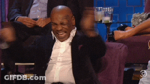 A Man In A Suit Is Sitting On A Couch With His Arms Outstretched And Laughing . GIF
