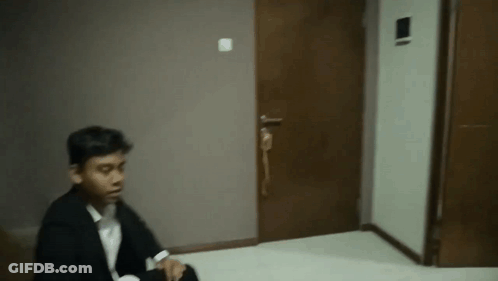 A Man In A Suit Is Sitting On The Floor In Front Of A Door In A Dark Room . GIF