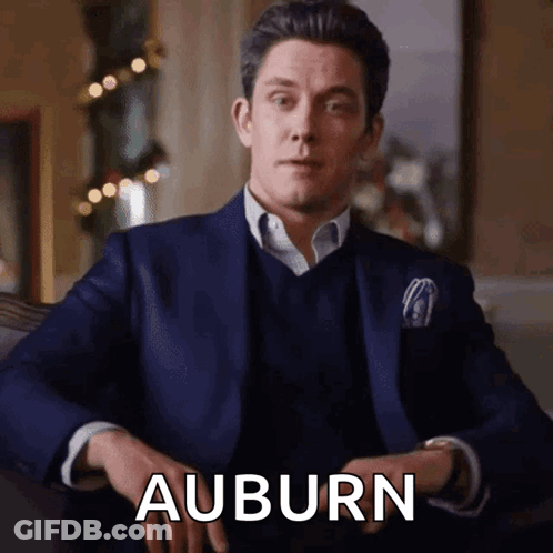 A Man In A Suit Is Sitting With His Hands Folded And The Word Auburn Is Visible GIF