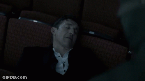 A Man In A Suit Is Sleeping In A Dark Auditorium Seat GIF