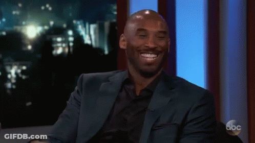 A Man In A Suit Is Smiling And Clapping His Hands While Sitting On A Stage . GIF