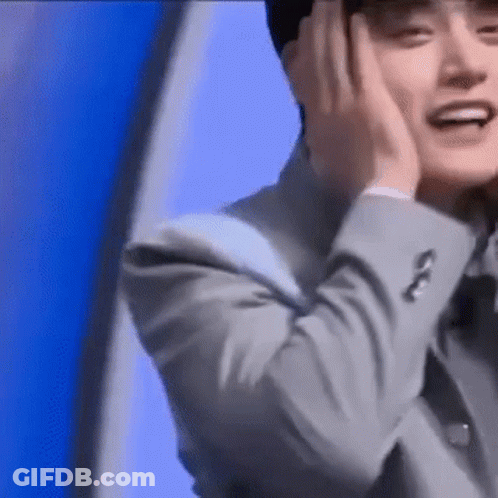 A Man In A Suit Is Smiling And Covering His Ears With His Hands . GIF