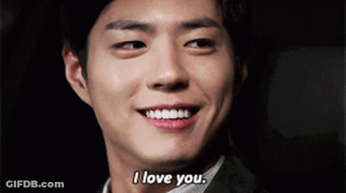 A Man In A Suit Is Smiling And Saying I Love You . GIF