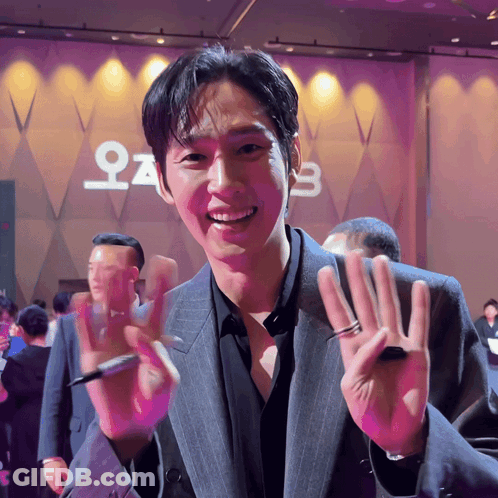 A Man In A Suit Is Smiling In Front Of A Sign That Says ' O ' On It GIF