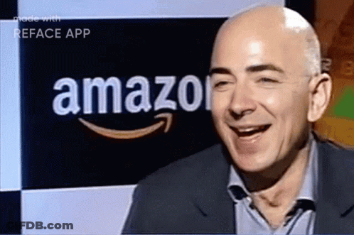 A Man In A Suit Is Smiling In Front Of An Amazon Logo GIF