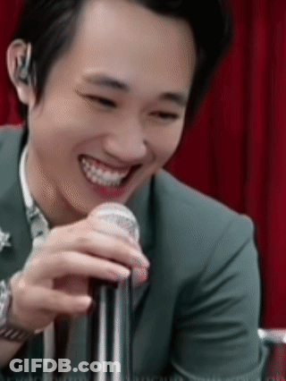 A Man In A Suit Is Smiling While Holding A Microphone In His Hand . GIF