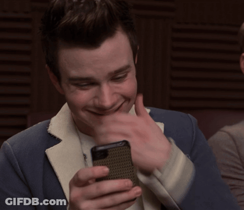 A Man In A Suit Is Smiling While Looking At His Cell Phone GIF