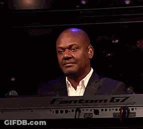 A Man In A Suit Is Smiling While Sitting At A Keyboard . GIF