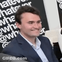 A Man In A Suit Is Smiling While Sitting In Front Of A Sign That Says `` What Do You Hate ? '' GIF