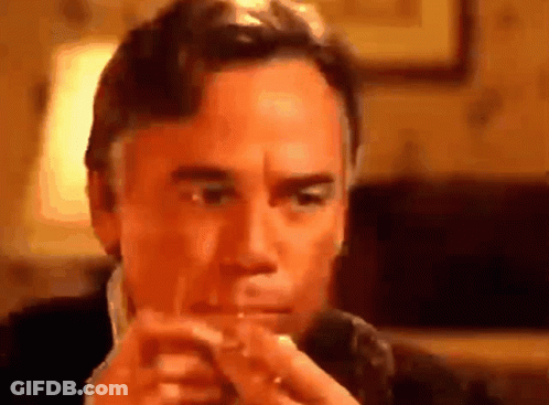 A Man In A Suit Is Smoking A Cigarette In A Room . GIF