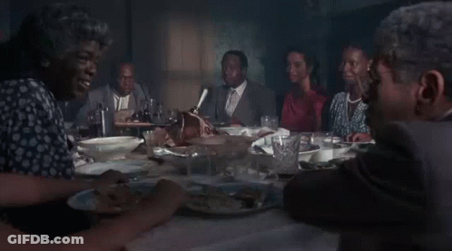 A Man In A Suit Is Smoking A Cigarette While Sitting At A Table With A Woman . GIF