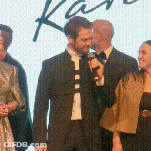 A Man In A Suit Is Speaking Into A Microphone While Standing Next To A Woman GIF