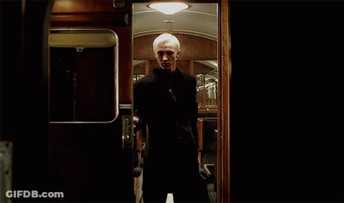 A Man In A Suit Is Standing In A Dark Room Behind A Door . GIF