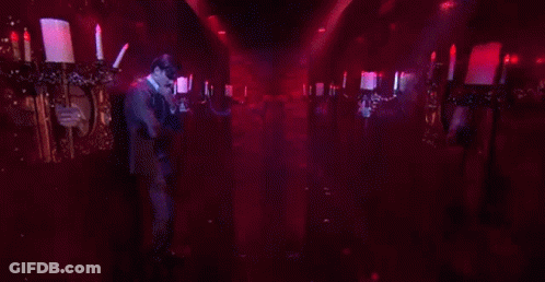 A Man In A Suit Is Standing In A Dark Room Holding A Candle . GIF