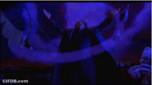 A Man In A Suit Is Standing In A Dark Room With His Arms Outstretched In The Air . GIF