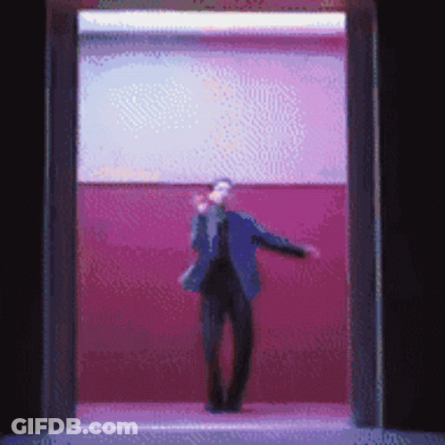 A Man In A Suit Is Standing In A Doorway With A Pink Wall Behind Him GIF