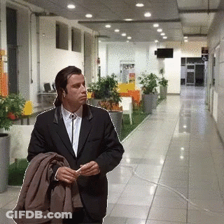 A Man In A Suit Is Standing In A Hallway Holding A Jacket GIF