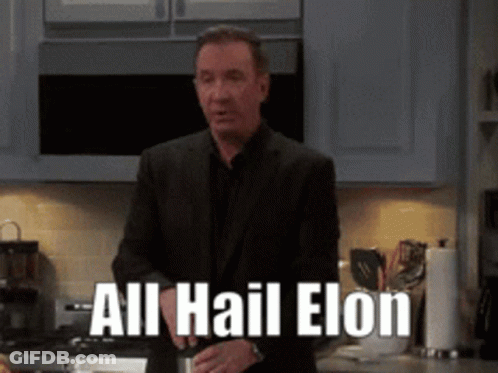 A Man In A Suit Is Standing In A Kitchen With The Words All Hail Elon On The Counter GIF