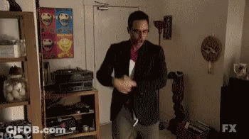 A Man In A Suit Is Standing In A Living Room With A Sign That Says Fx On It . GIF