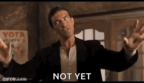 A Man In A Suit Is Standing In A Room With His Arms Outstretched And A Sign That Says Not Yet . GIF