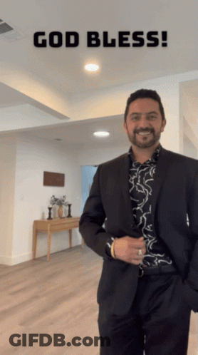 A Man In A Suit Is Standing In A Room With The Words God Bless Written Above Him GIF