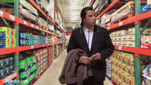 A Man In A Suit Is Standing In A Store Aisle With A Sign That Says ' Pri ' On It GIF