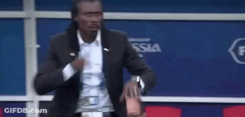A Man In A Suit Is Standing In Front Of A Blue Wall And Holding A Bottle Of Water . GIF