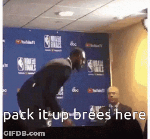 A Man In A Suit Is Standing In Front Of A Blue Wall With The Words Pack It Up Brees Here Written On It . GIF
