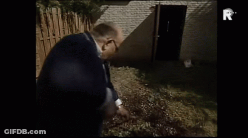 A Man In A Suit Is Standing In Front Of A Brick Building With The Letter R On The Bottom Of The Screen GIF
