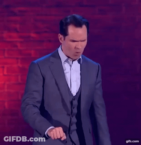 A Man In A Suit Is Standing In Front Of A Brick Wall And Making A Funny Face . GIF