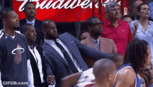 A Man In A Suit Is Standing In Front Of A Budweiser Sign . GIF