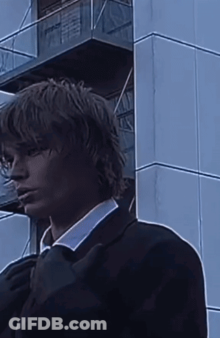 A Man In A Suit Is Standing In Front Of A Building . GIF