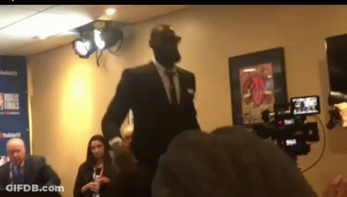 A Man In A Suit Is Standing In Front Of A Camera In A Room GIF