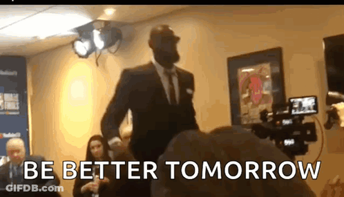A Man In A Suit Is Standing In Front Of A Camera With The Words Be Better Tomorrow Written On The Bottom GIF