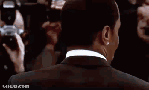 A Man In A Suit Is Standing In Front Of A Crowd Of People And A Camera . GIF