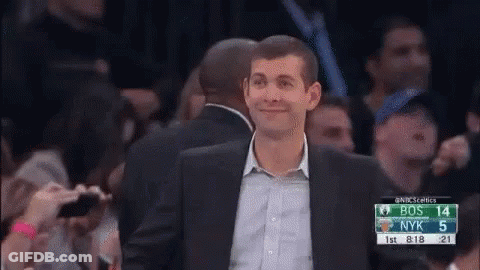 A Man In A Suit Is Standing In Front Of A Crowd Watching A Basketball Game Between Bos And Nyk . GIF