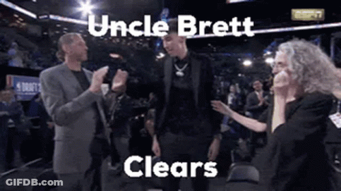 A Man In A Suit Is Standing In Front Of A Crowd With The Words Uncle Brett Clears Written Above Him . GIF