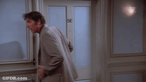 A Man In A Suit Is Standing In Front Of A Door That Says 5E GIF