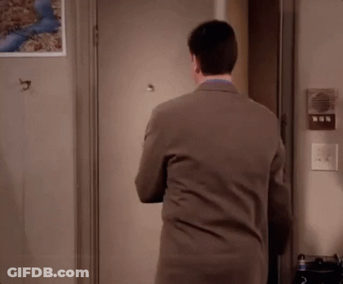 A Man In A Suit Is Standing In Front Of A Door With His Arms Crossed . GIF